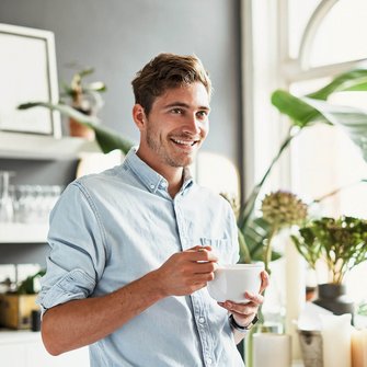 Ein Mann steht mit einer Tasse in der Hand in seiner Küche.