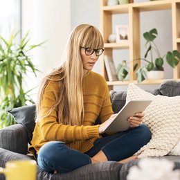 Eine junge Frau sitzt mit ihrem Tablet auf dem Sofa.